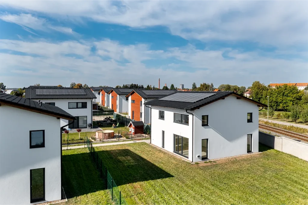 Letecký pohled na novostavby rodinných domů v Kostelci nad Labem s fotovoltaickými panely a oplocenými pozemky.