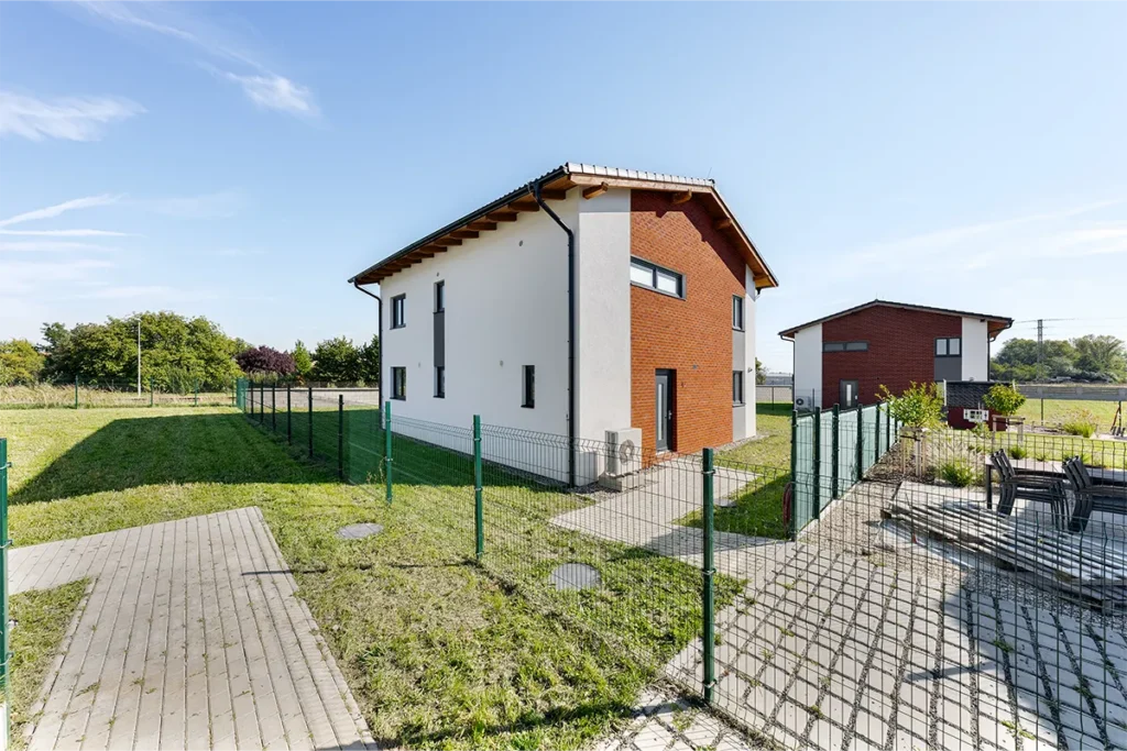 Moderní rodinný dům v Kostelci nad Labem s bílou a cihlovou fasádou, oplocenou zahradou a tepelným čerpadlem.