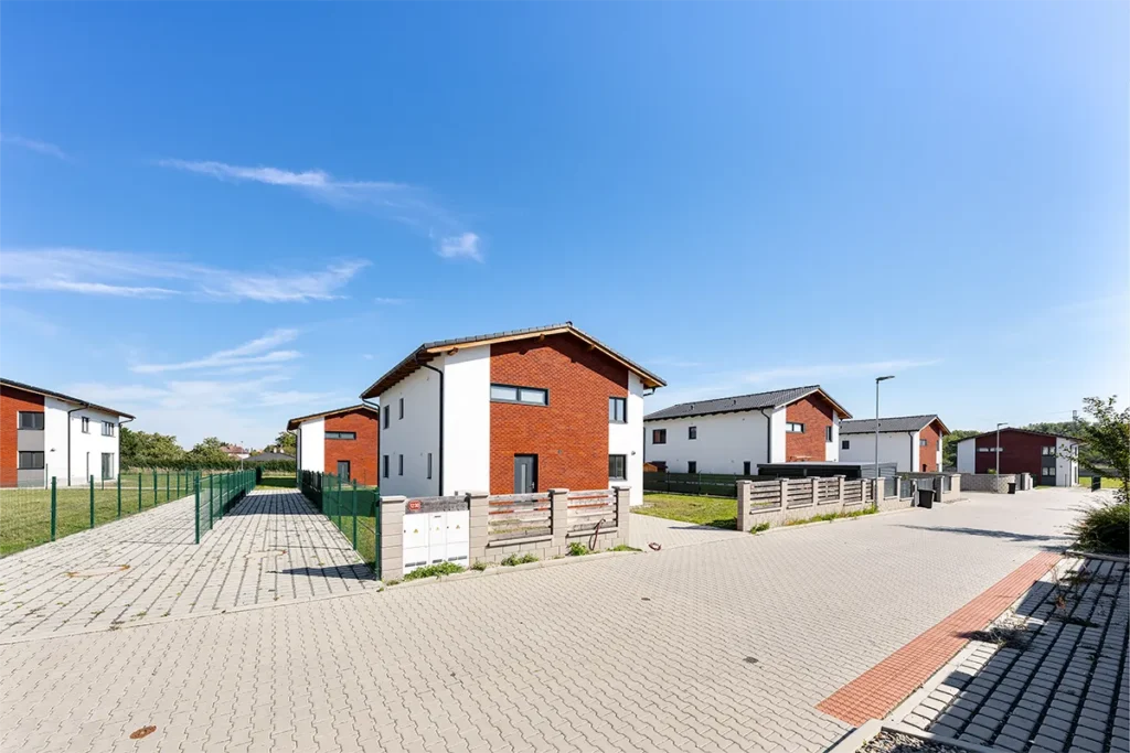 Pohled ze zahrady na moderní rodinný dům s francouzskými okny, bílou fasádou a prostorným pozemkem.